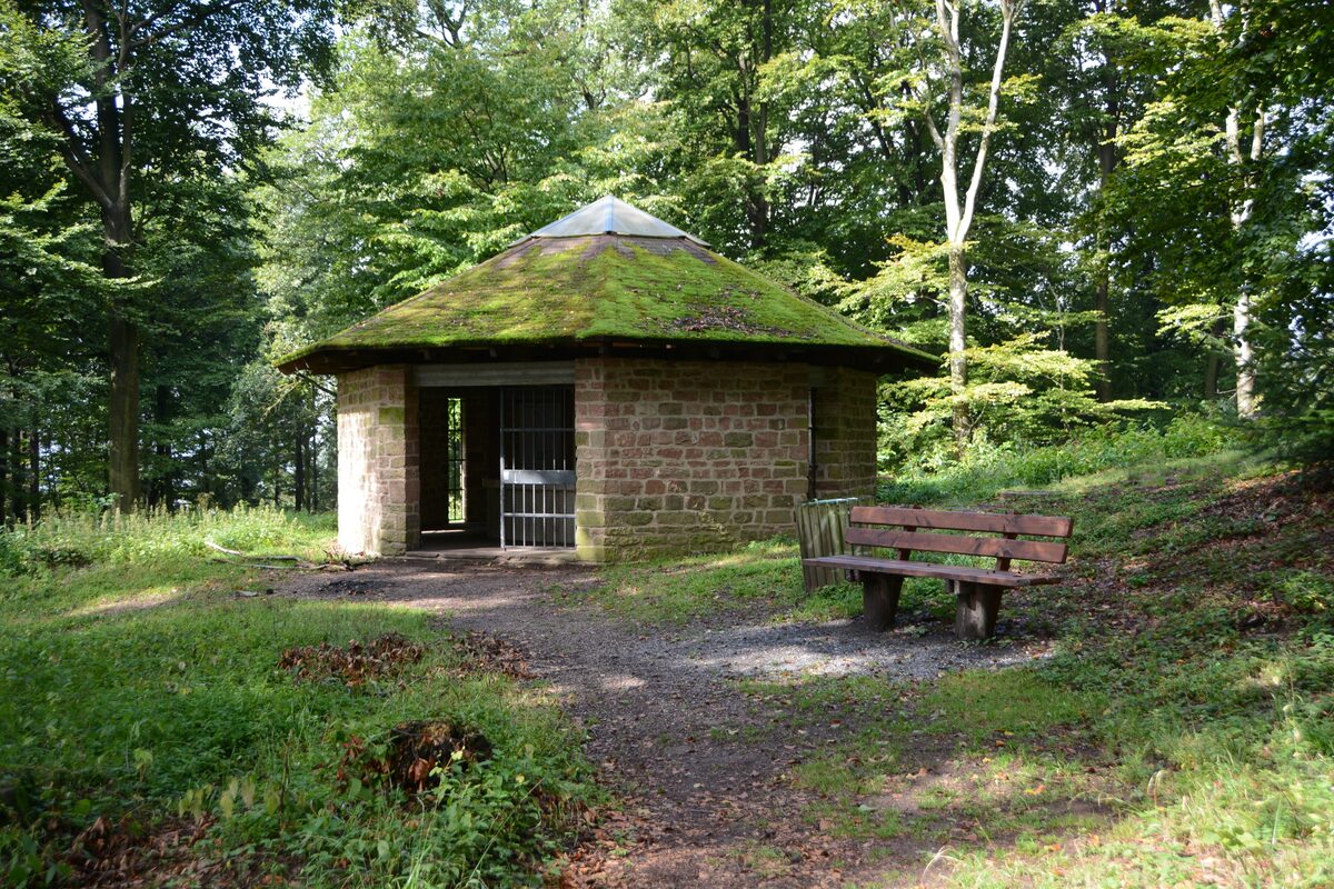 The small stone hut over the Heidenloch shaft on the Heiligenberg, in the forest with a bench in front