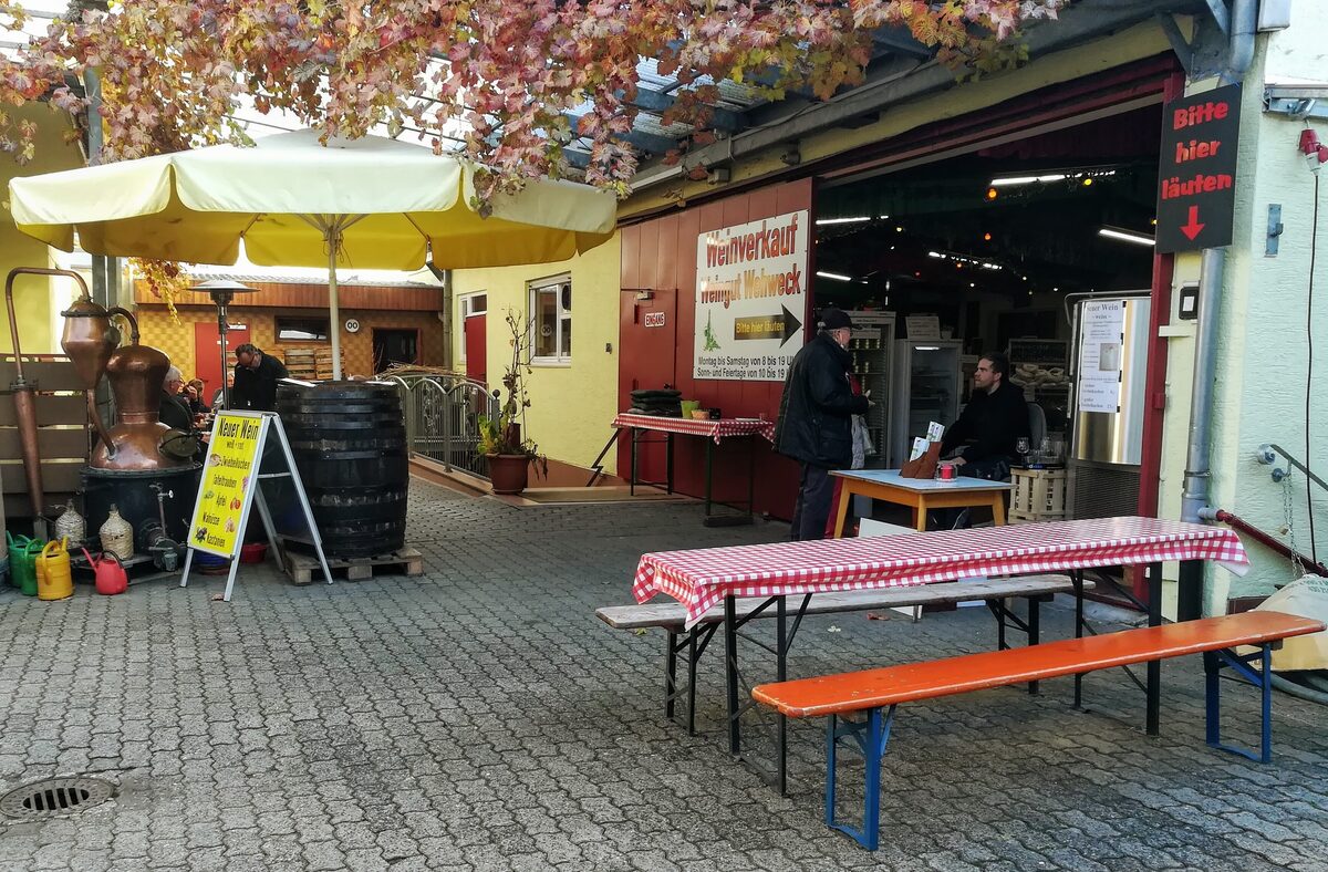 A winery courtyard in Schriesheim with benches, a copper still and a sign for new wine