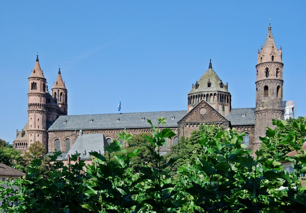 The towers and domes of Worms Cathedral in the sun, seen over a hedge