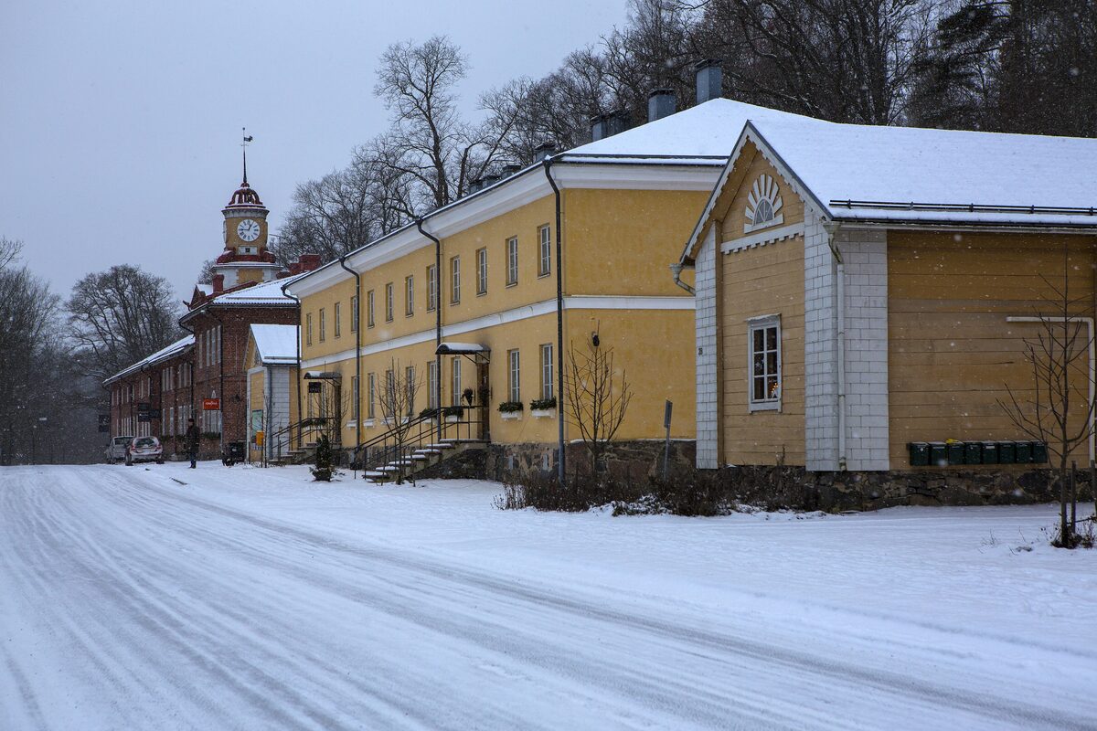 Yellow and white old ironworks buildings with a clock tower along a snowy street in Fiskars village