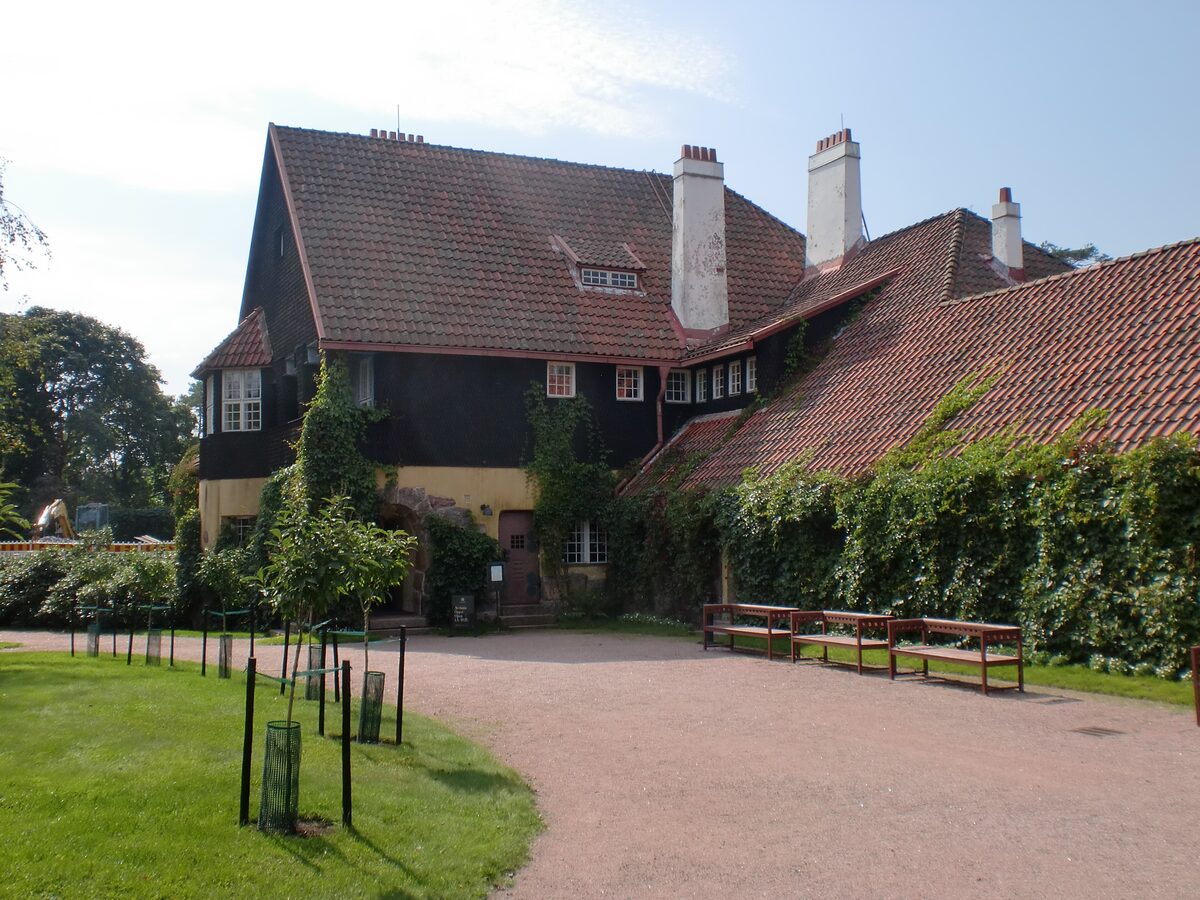 The dark log and stone studio home of Hvitträsk with steep red tile roofs and a lawn in front