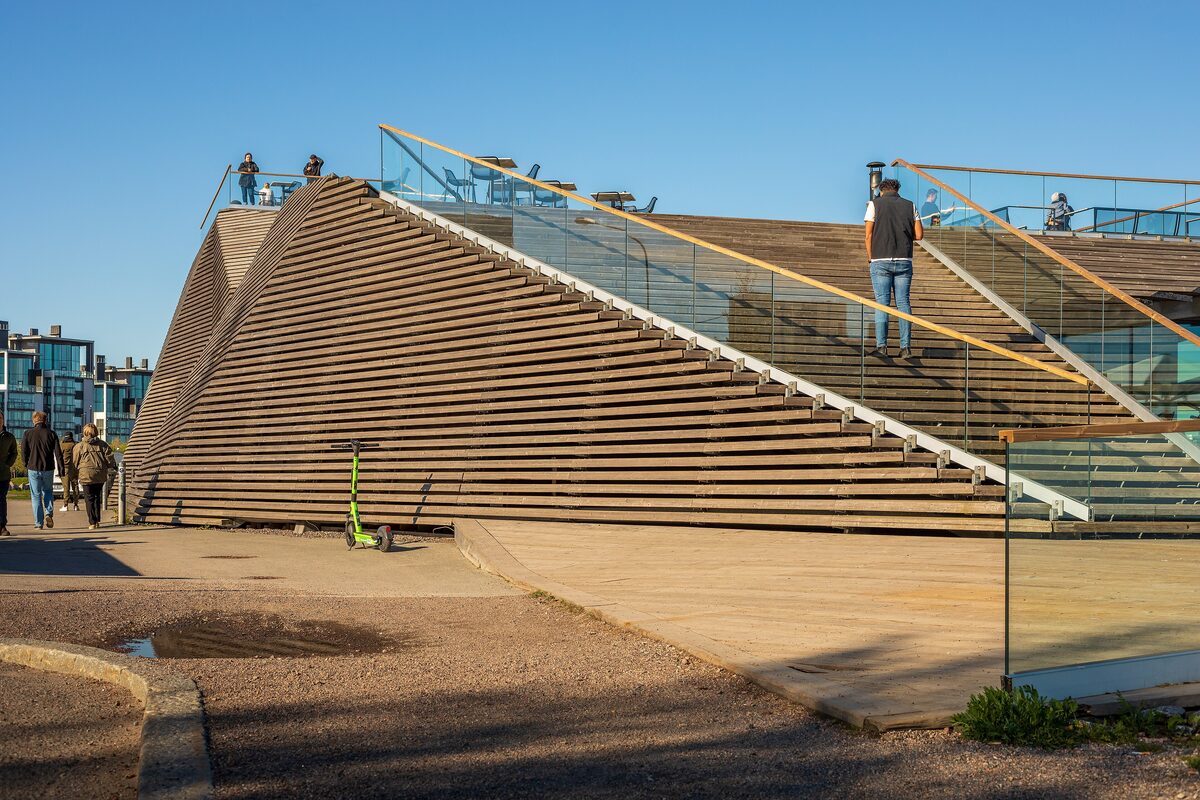 The angular wooden slats of the Löyly sauna building on the seafront, with people walking up its outdoor stairs