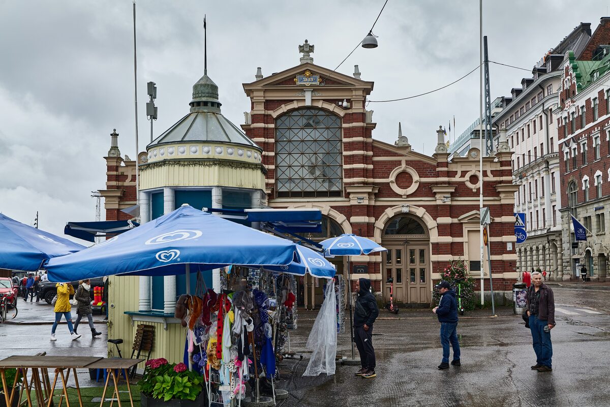 Market stalls under blue umbrellas in front of the red and yellow brick Old Market Hall on Helsinki's South Harbor