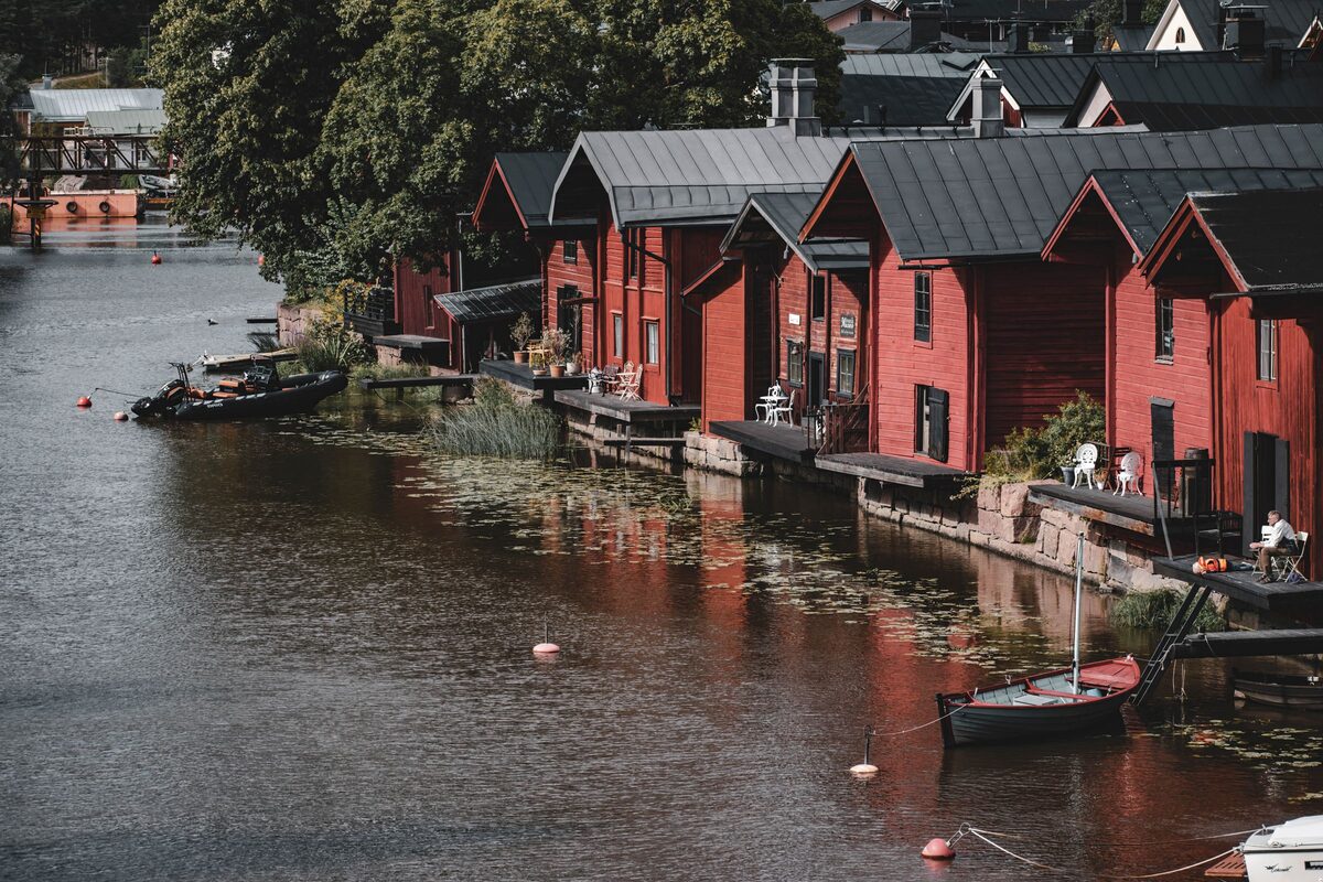 A row of red wooden riverside storehouses in Porvoo reflected in the river, with a rowing boat moored in front