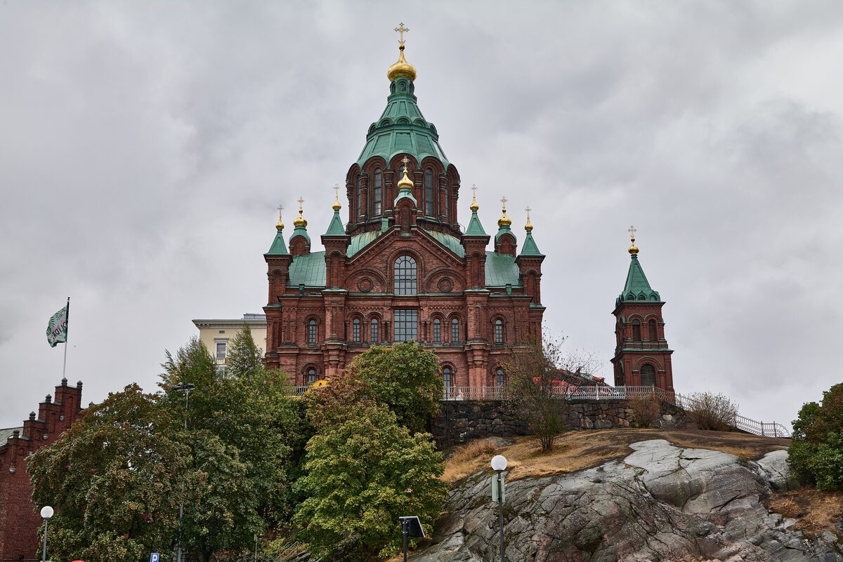 The red-brick Uspenski Cathedral with green roofs and golden onion domes on a rocky hill above trees