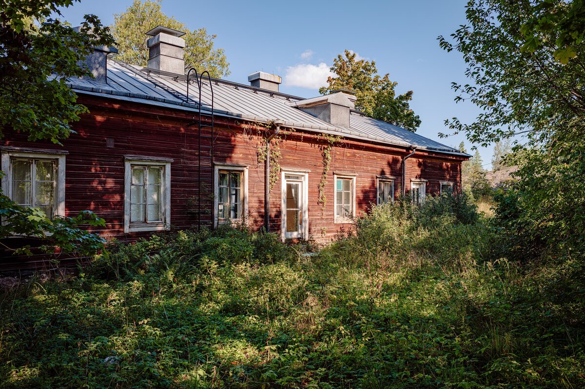 An old red wooden house among tall trees and bushes on the island of Vallisaari