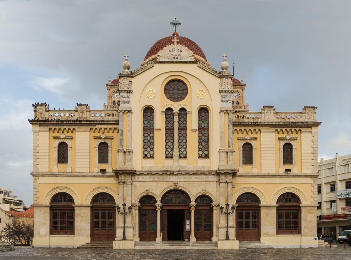 The facade of the cathedral of Agios Minas in Heraklion, a large cream and yellow church with a red dome and arched windows