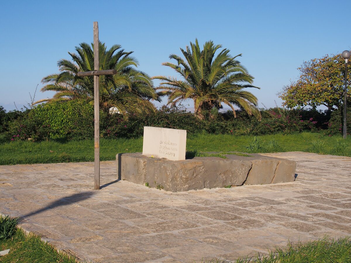 Nikos Kazantzakis's grave on the Martinengo bastion: a simple stone slab with a plain wooden cross beside it, under palm trees