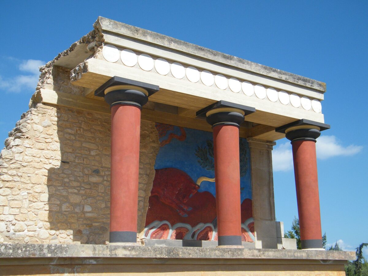 The reconstructed north entrance of Knossos, with red tapering Minoan columns and a fresco of a charging bull on the wall behind