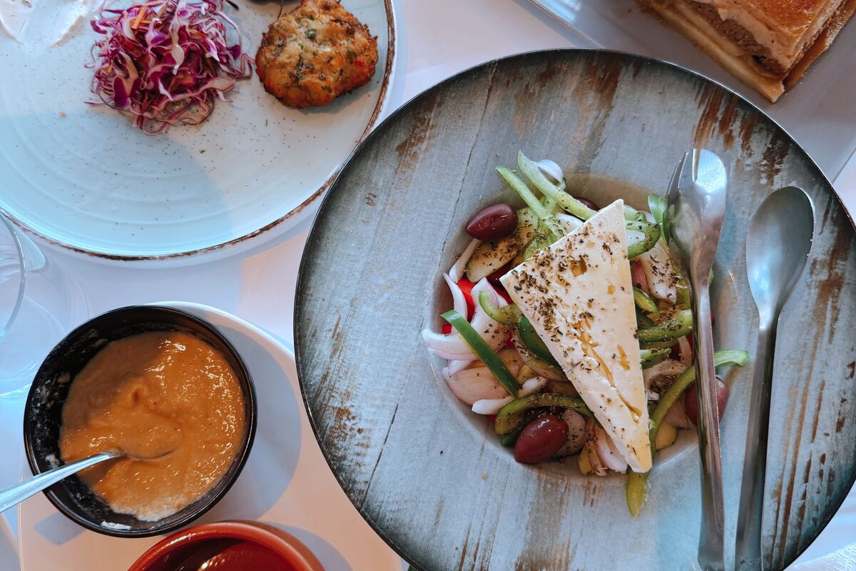 Overhead view of Greek meze: a salad with a slab of feta and olives, a bowl of fava and a fried fritter