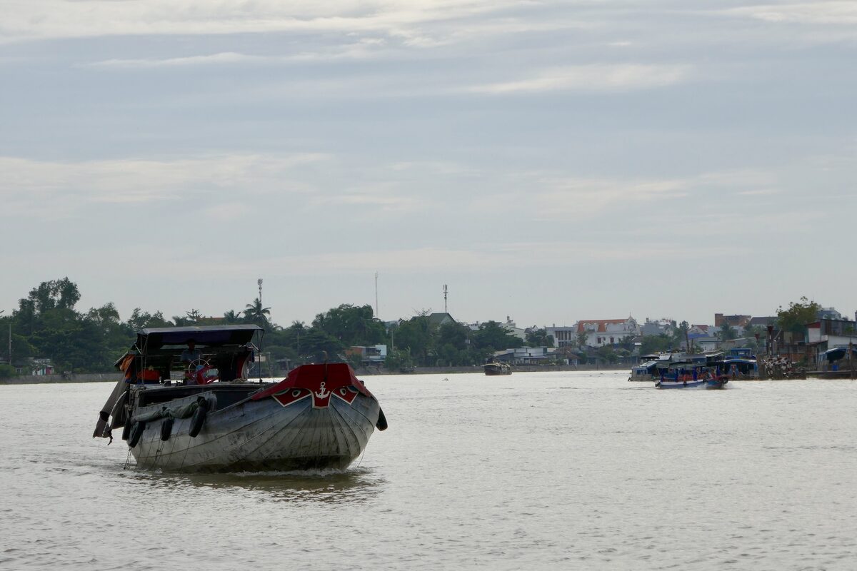 A wooden river boat on a wide brown river near Cần Thơ, with the far bank and boats in the distance