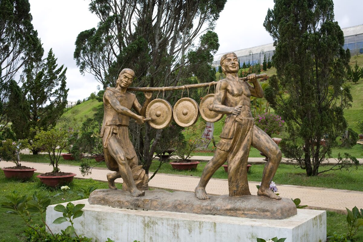Two bronze statues of figures carrying gongs in the Đà Lạt Flower Park