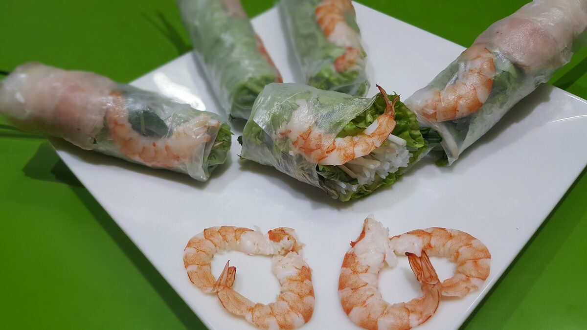 Fresh spring rolls filled with shrimp and herbs, with more shrimp on a white plate