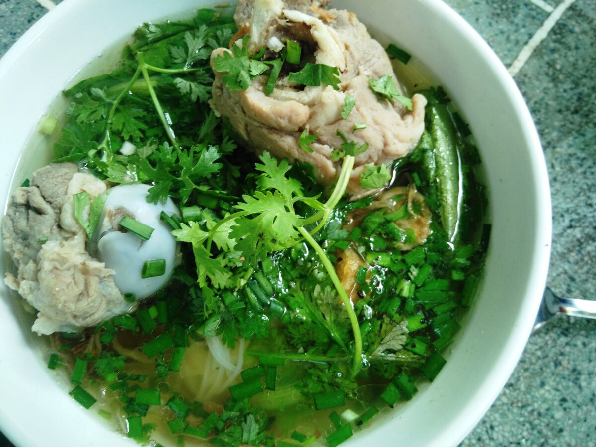 A bowl of hu tieu Nam Vang with pork, a quail egg and a pile of herbs on top