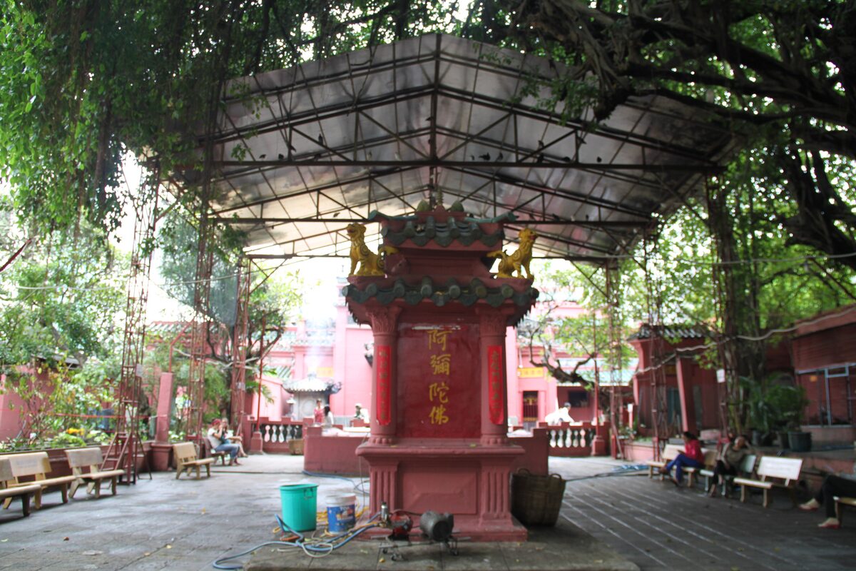 A red ornamental shrine with gold lions under a shelter and tree roots in the courtyard of the Jade Emperor Pagoda