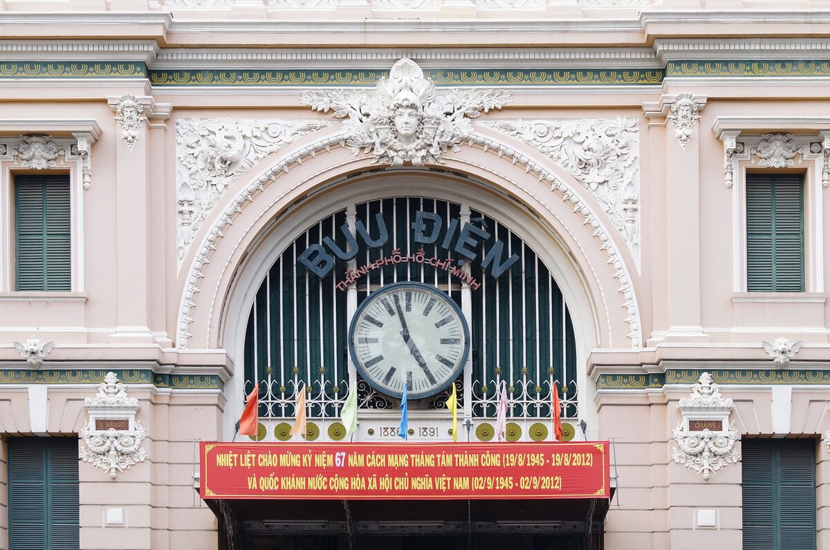 The clock arch of the pink Saigon Central Post Office with its Bưu Điện sign and a red banner below the clock