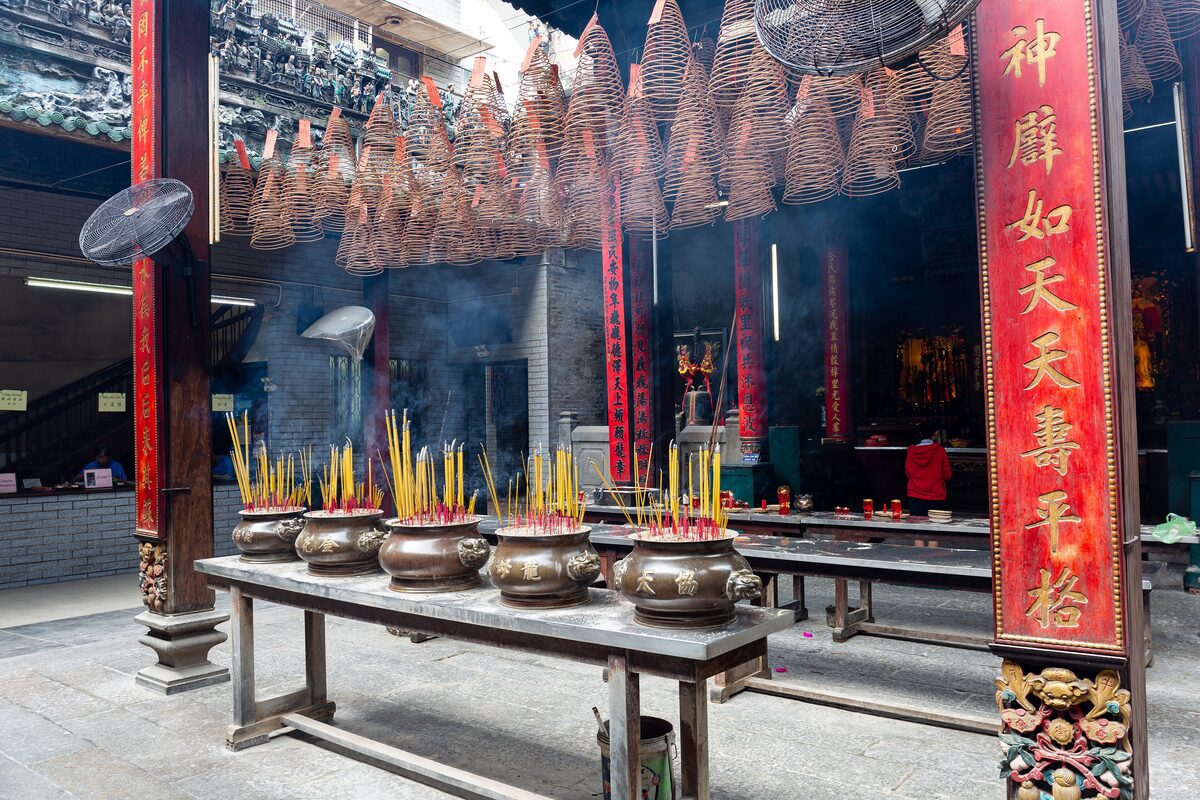 Spiral incense coils hanging over the main hall of Thiên Hậu Temple, with burners of incense sticks on a table in front