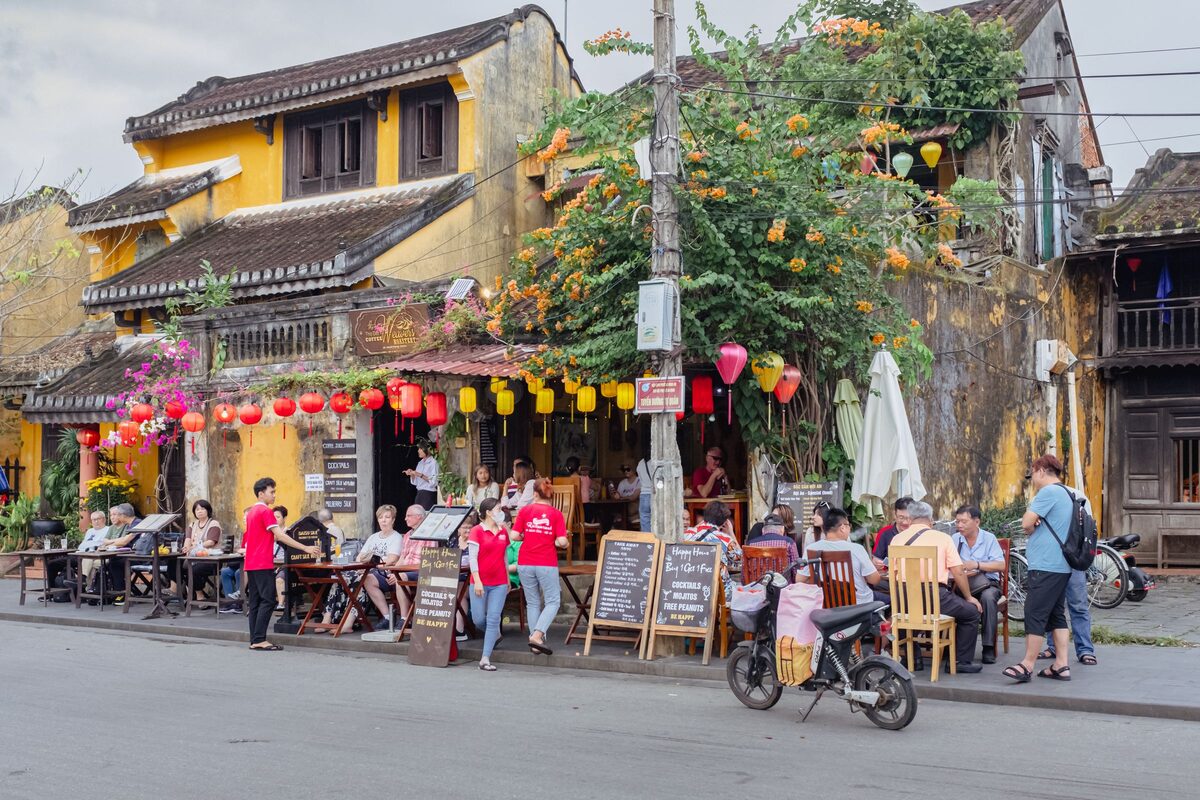 Street-level outdoor cafe tables on a corner of an Ancient Town street, yellow walls, flowers and hanging lanterns behind the diners