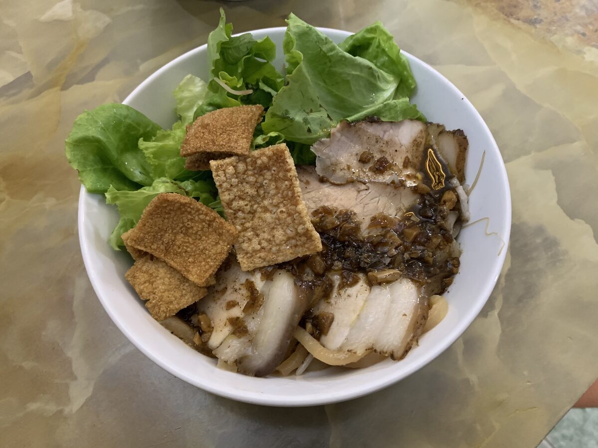 A bowl of cao lau with pork, crisp noodle croutons and herbs