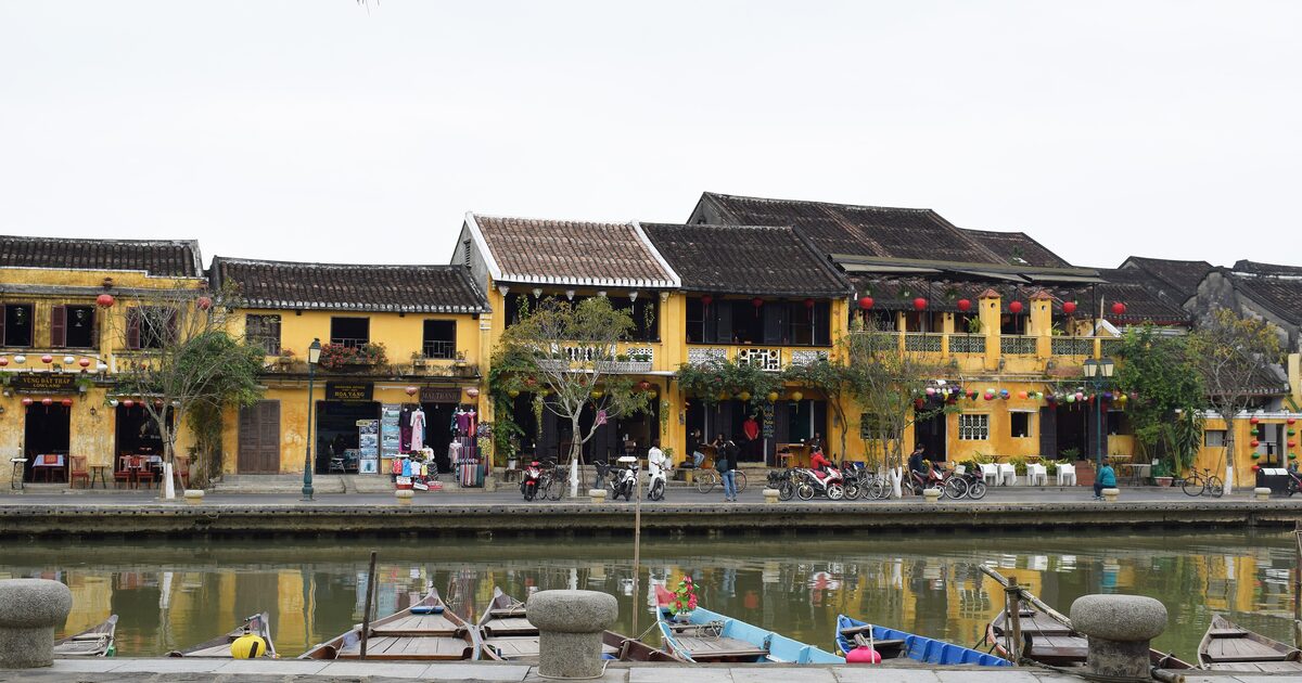 Yellow merchant houses with red lanterns along the Thu Bon riverfront in Hoi An Ancient Town, with wooden boats moored at the quay