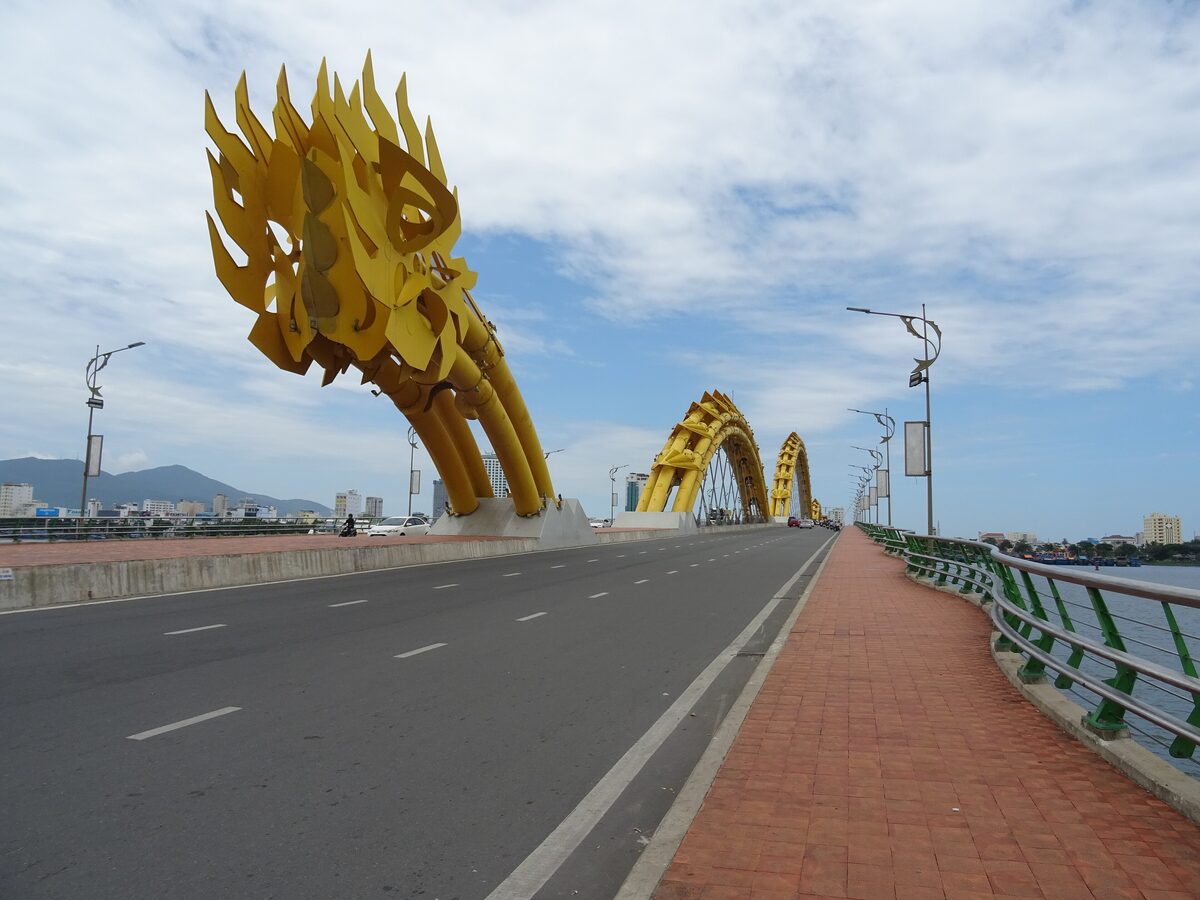 The golden dragon head of the Dragon Bridge in Da Nang, with the bridge arching behind it