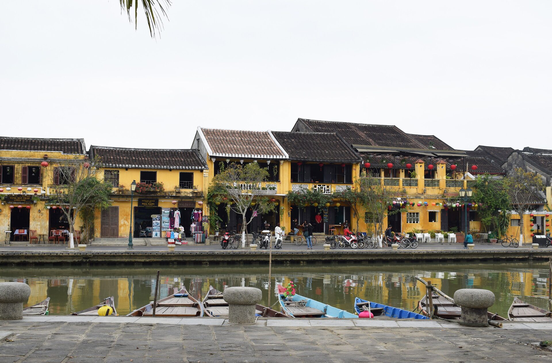 Yellow merchant houses with red lanterns along the Thu Bon riverfront in Hoi An Ancient Town, with wooden boats moored at the quay