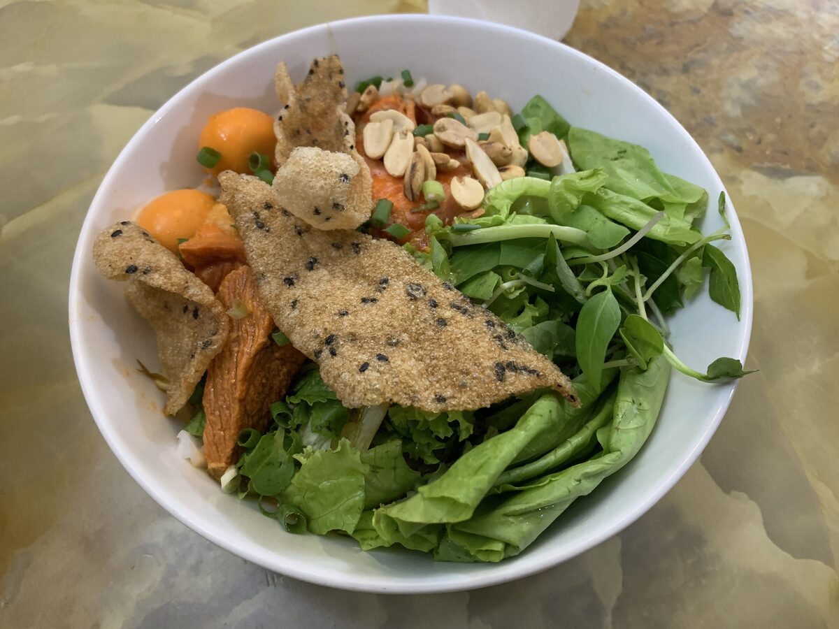 A bowl of mi quang with turmeric noodles, peanuts, crackers and herbs