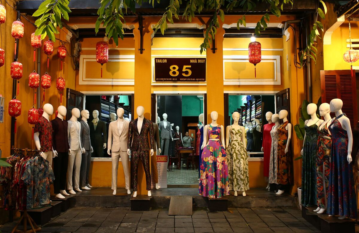 A tailor shopfront in the Ancient Town at night, lanterns hanging over rows of mannequins in suits and dresses