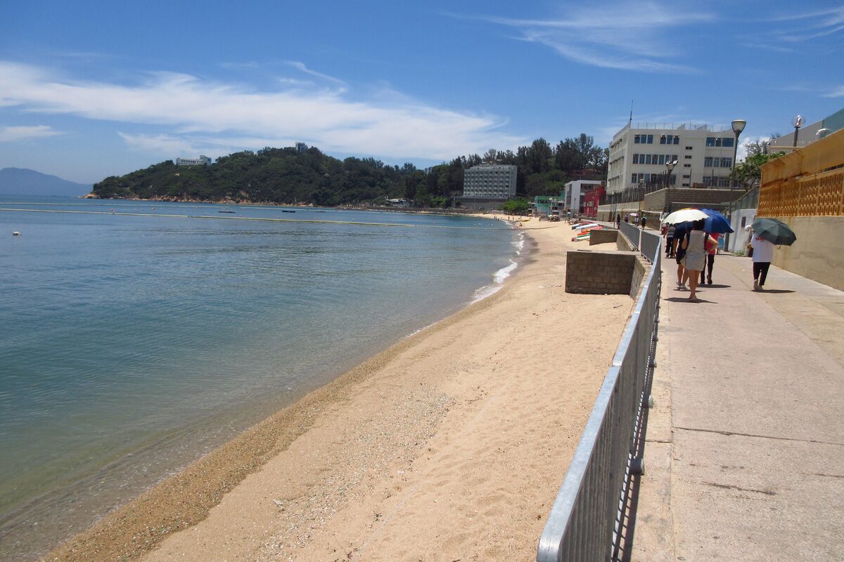 Tung Wan Beach on Cheung Chau under a blue sky, with a strip of sand, clear water and a green headland beyond