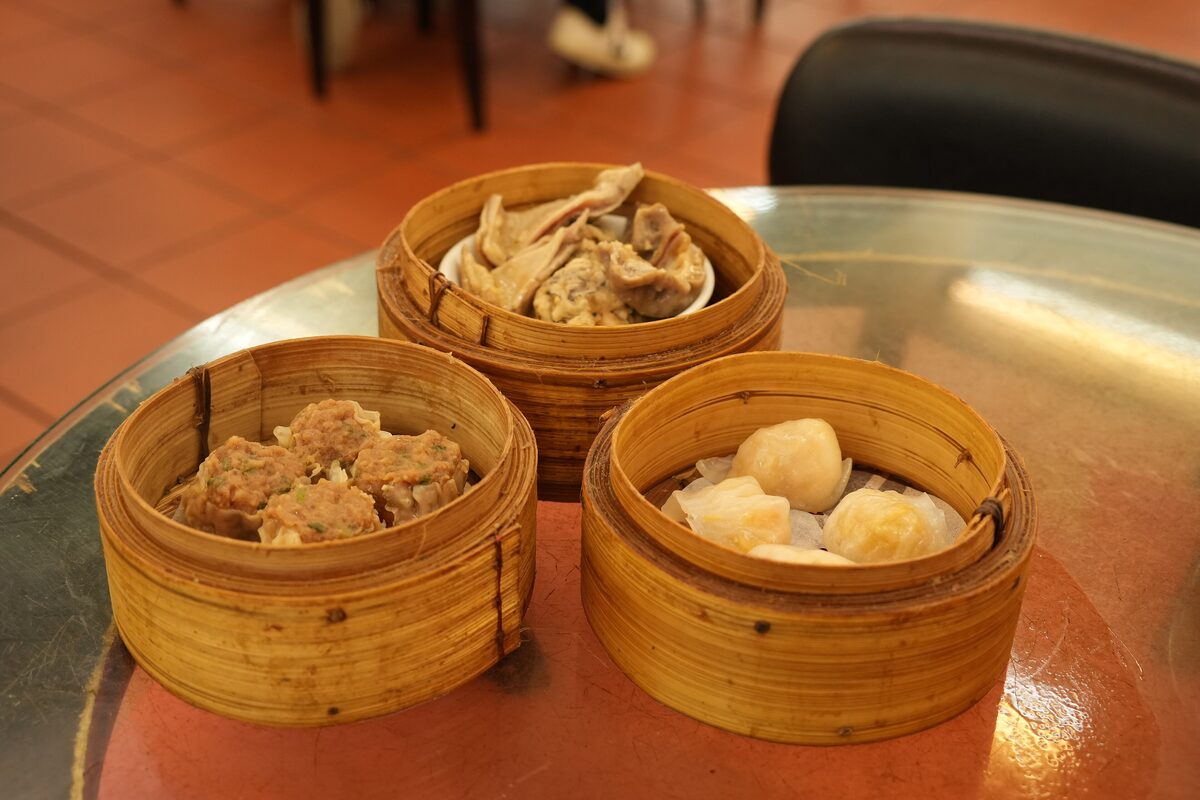 Three bamboo steamers of dim sum on a table, holding meat dumplings, a braised dish and translucent shrimp dumplings