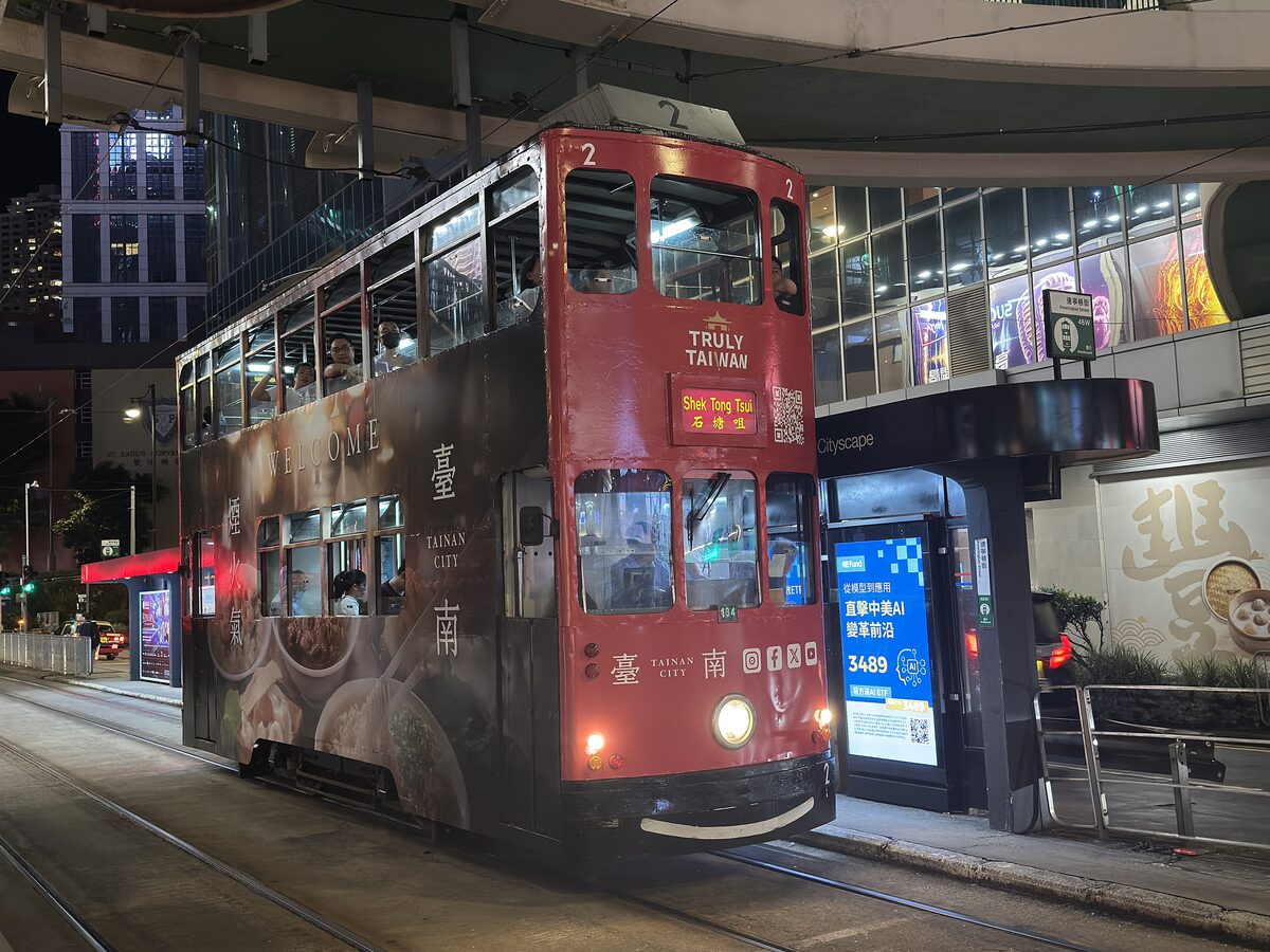 A red double-decker Hong Kong tram stopped at a street-level stop at night