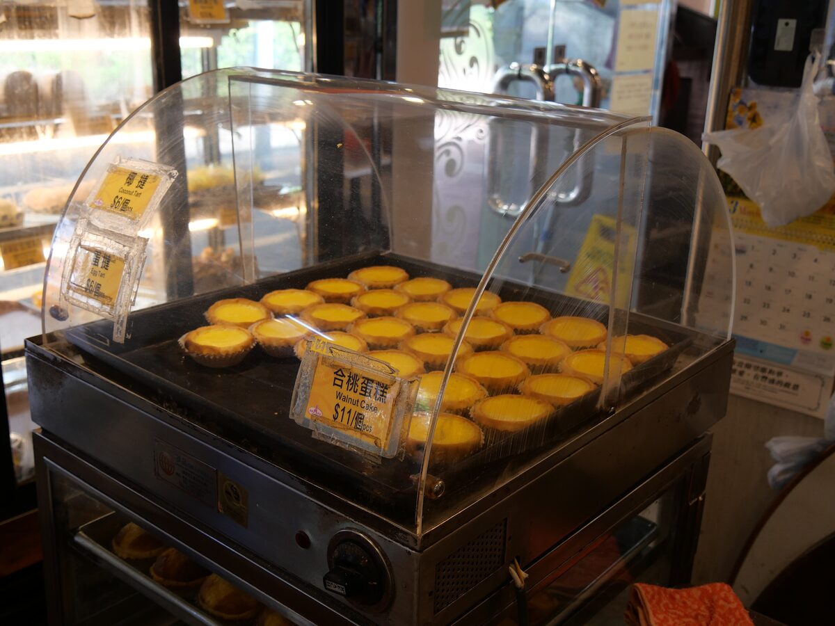 A tray of freshly baked Hong Kong-style egg tarts in a bakery display case
