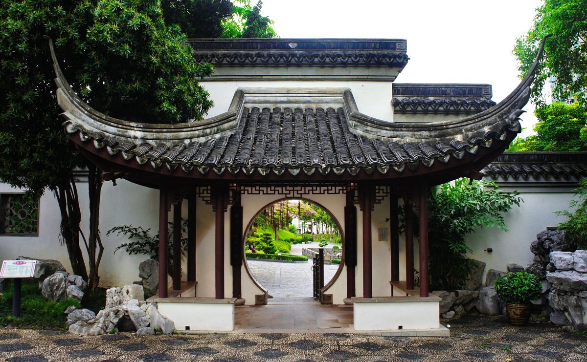 A Jiangnan-style garden pavilion with a round moon gate and curved tiled roof in Kowloon Walled City Park
