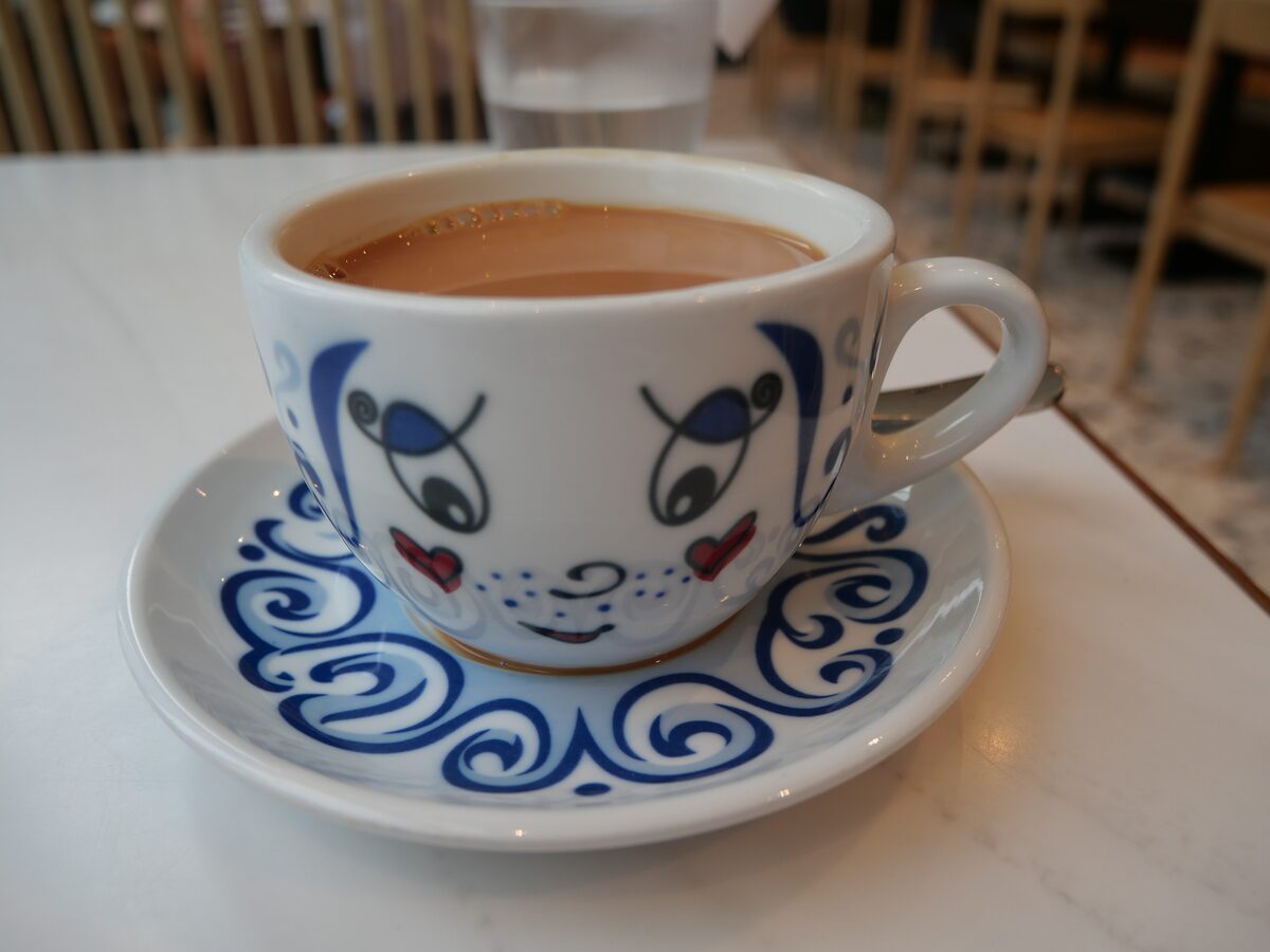 A cup of Hong Kong-style milk tea in a white cup and saucer with a blue swirl pattern and a small cartoon face