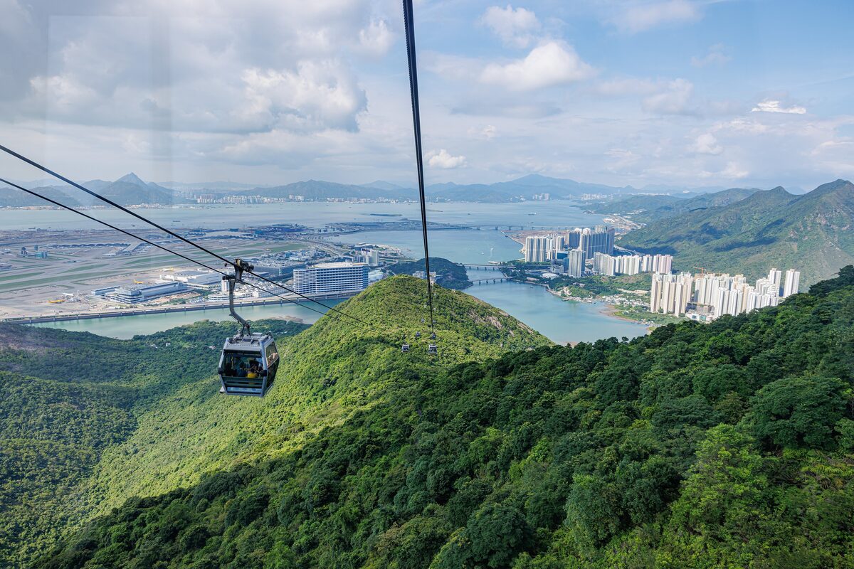 A Ngong Ping 360 cabin crossing green Lantau hills with the airport and the bay in the distance