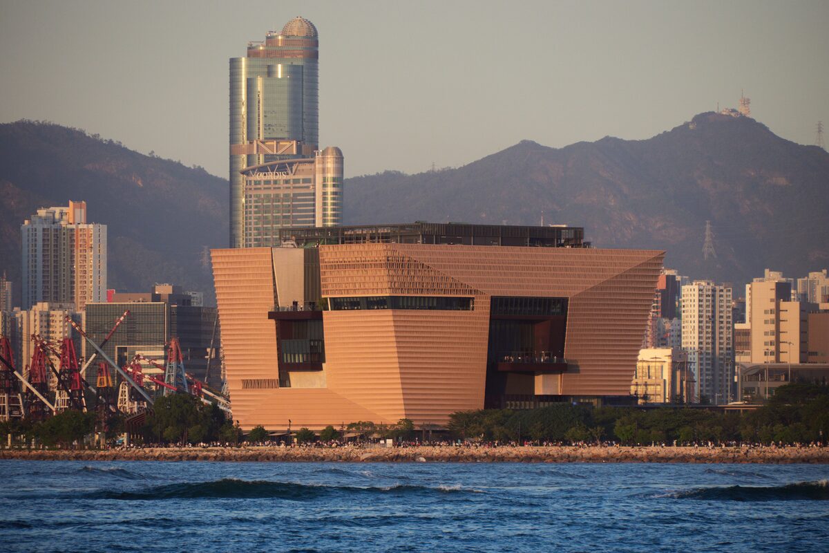 The Hong Kong Palace Museum on the West Kowloon waterfront in warm evening light, with hills behind