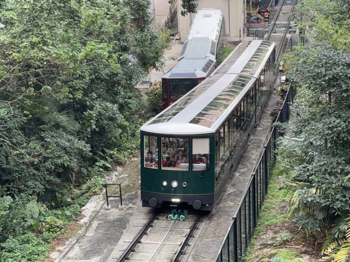 The green Peak Tram car climbing its steep track through the trees above the city