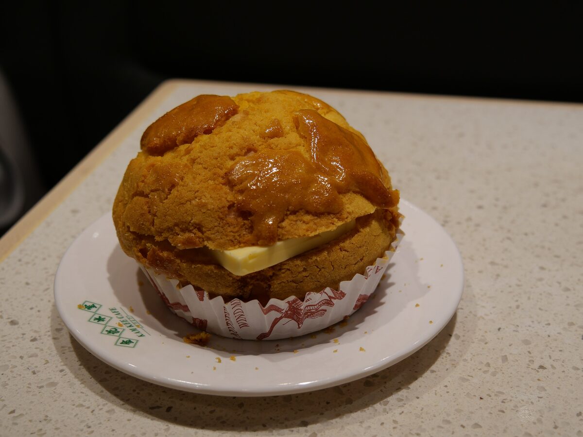 A pineapple bun with a golden crackled crust and a slab of butter inside, on a small plate