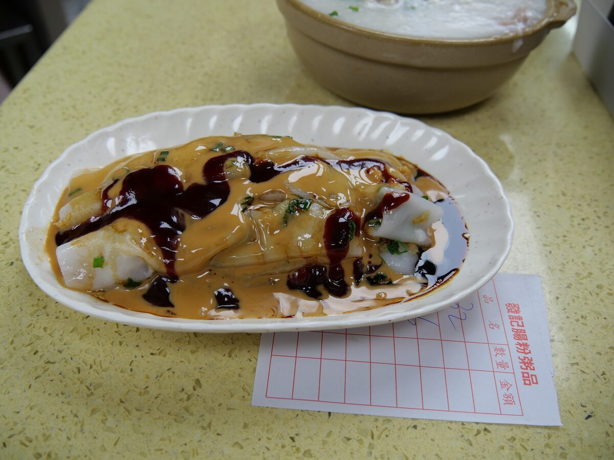 Steamed rice noodle rolls topped with peanut sauce, soy sauce and spring onion on an oval plate
