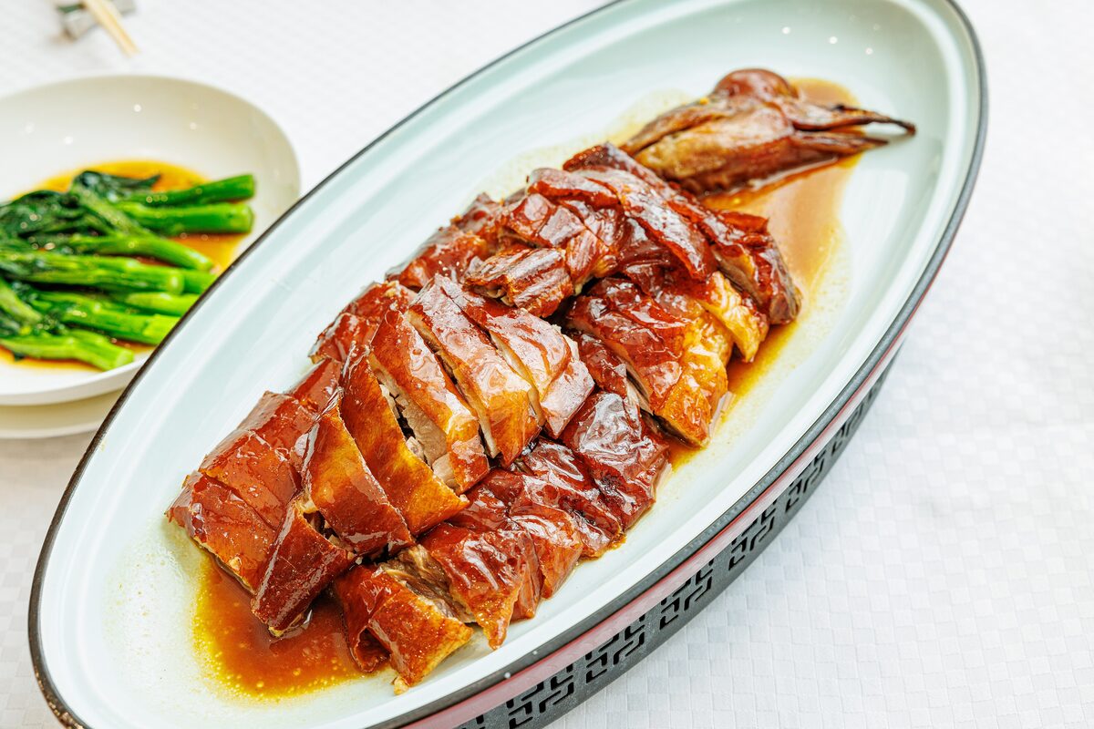 Chopped Cantonese roast goose with glossy brown skin on an oval plate, served with greens