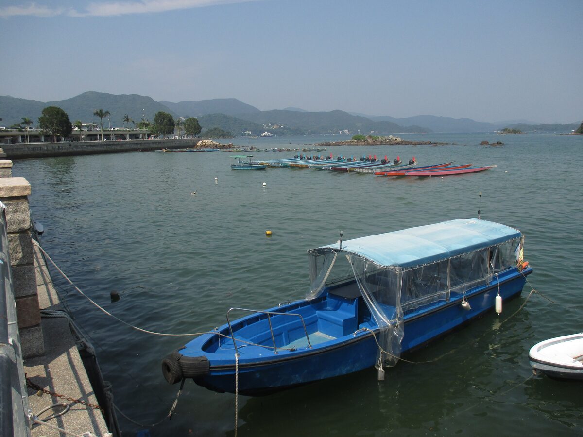 A blue boat moored at the Sai Kung waterfront with the bay and green hills behind