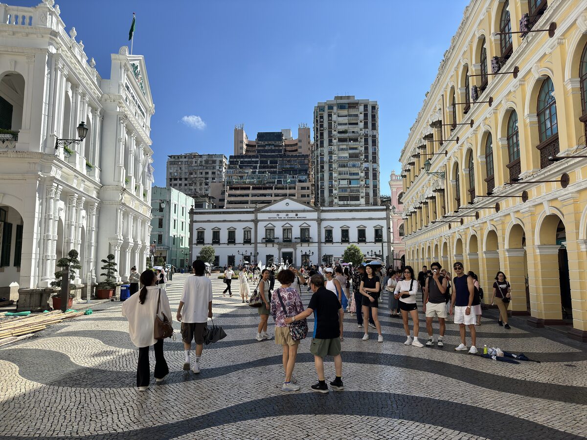 Visitors on Senado Square's wave-patterned black and white pavement between white and yellow colonial buildings