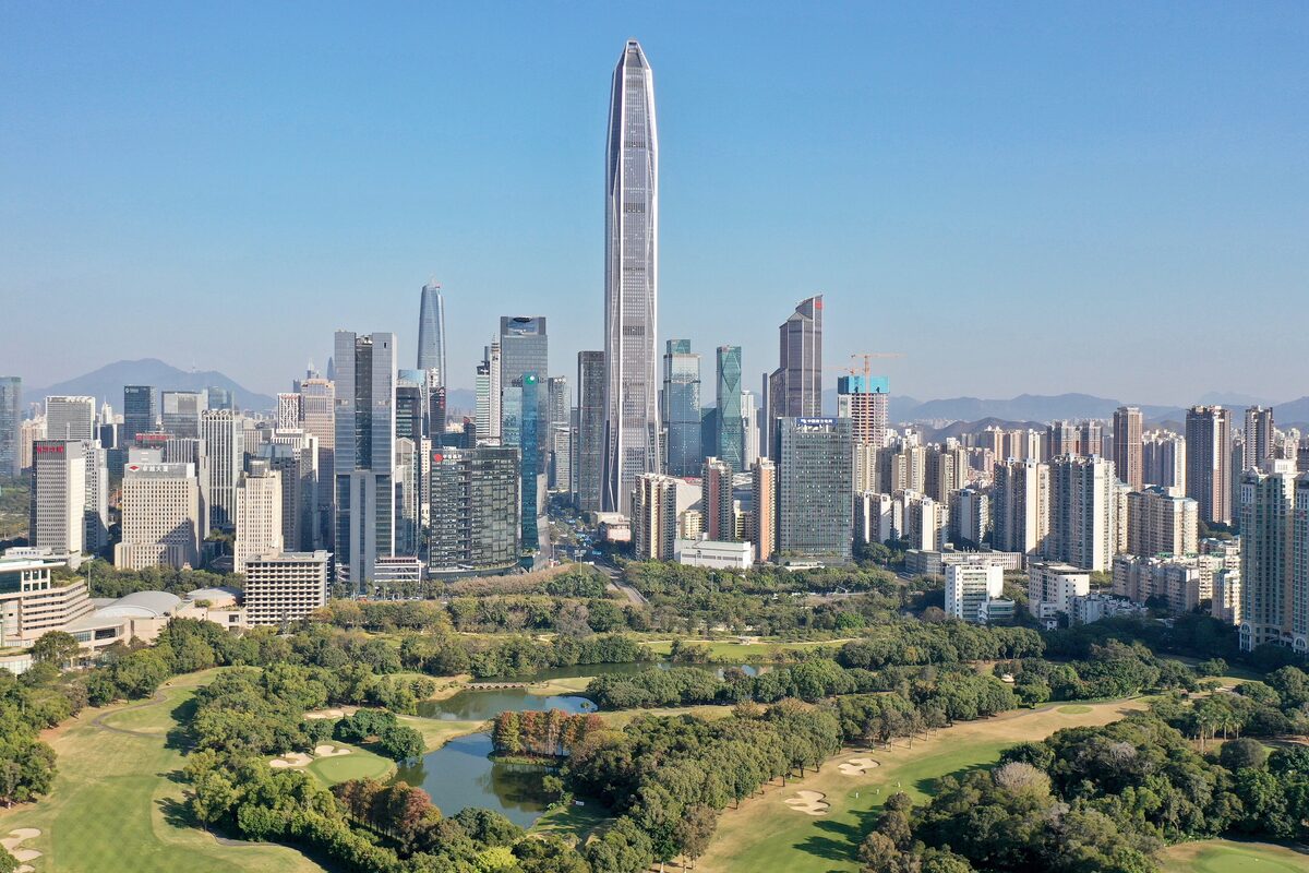 The Futian skyline of Shenzhen with a very tall tower rising over a green park and golf course