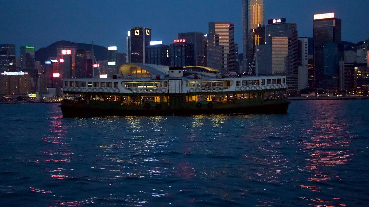 A Star Ferry crossing Victoria Harbour at night with the Central skyline lit up behind it