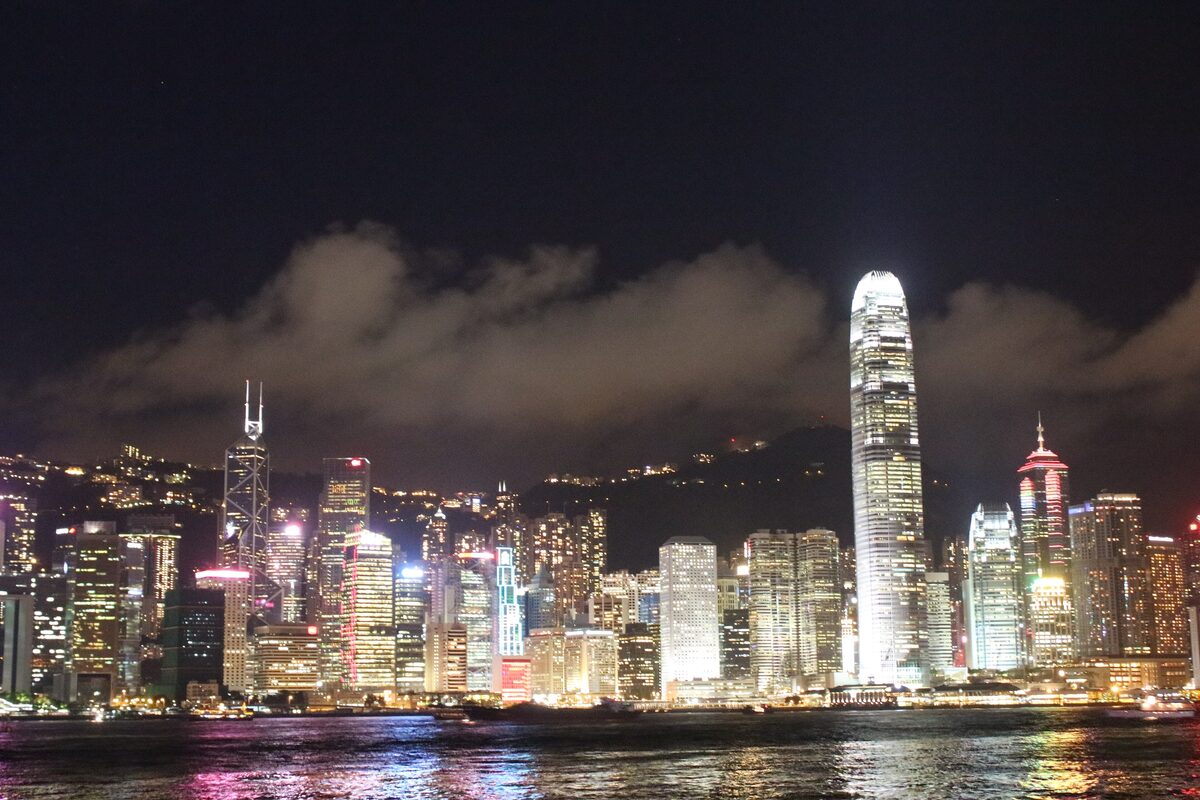 The lit-up Hong Kong Island skyline at night across Victoria Harbour, with the Two IFC tower glowing on the right