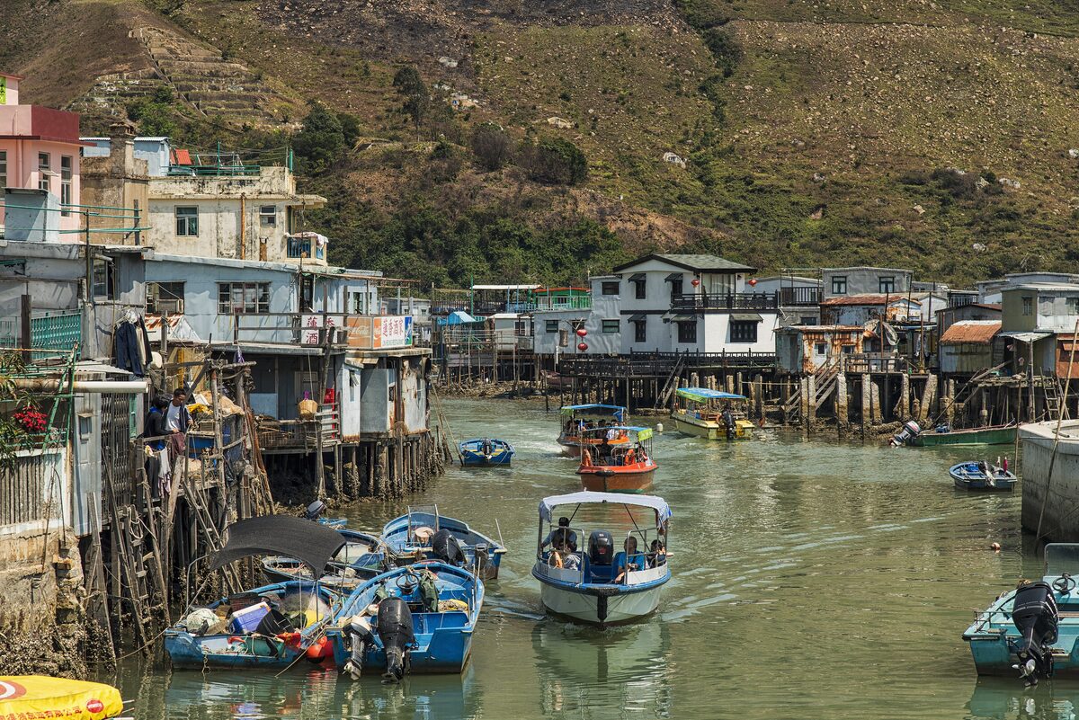 Stilt houses along the creek in Tai O with small boats on the water and a green hillside behind