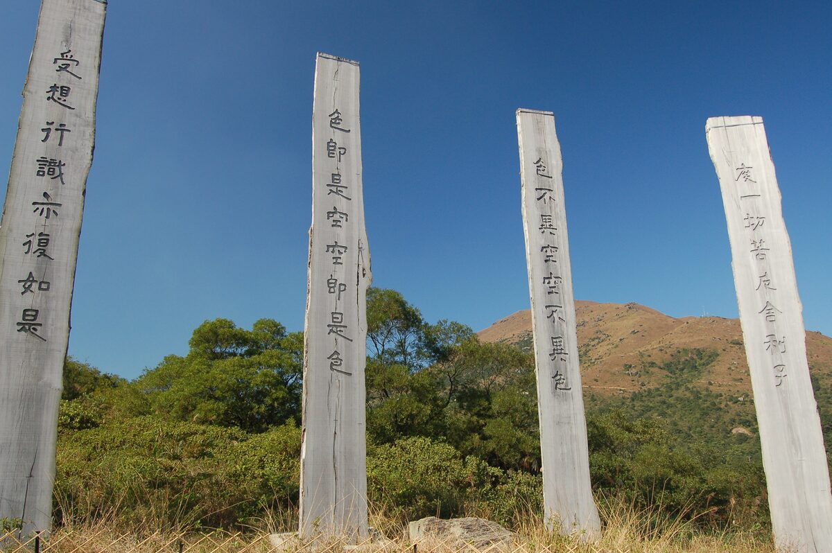Tall wooden posts inscribed with Heart Sutra characters on the Wisdom Path, with a hill behind