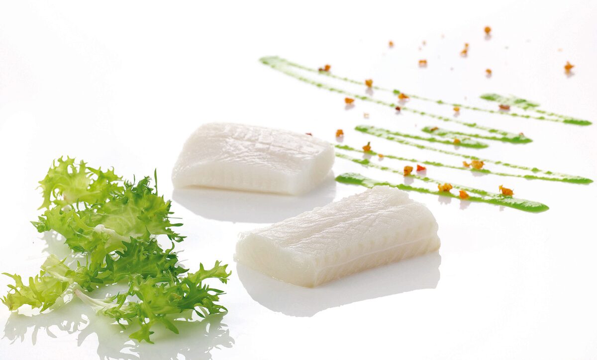 Two pale fillets of Greenland halibut on a white plate with frilly green herbs and a few dots of sauce
