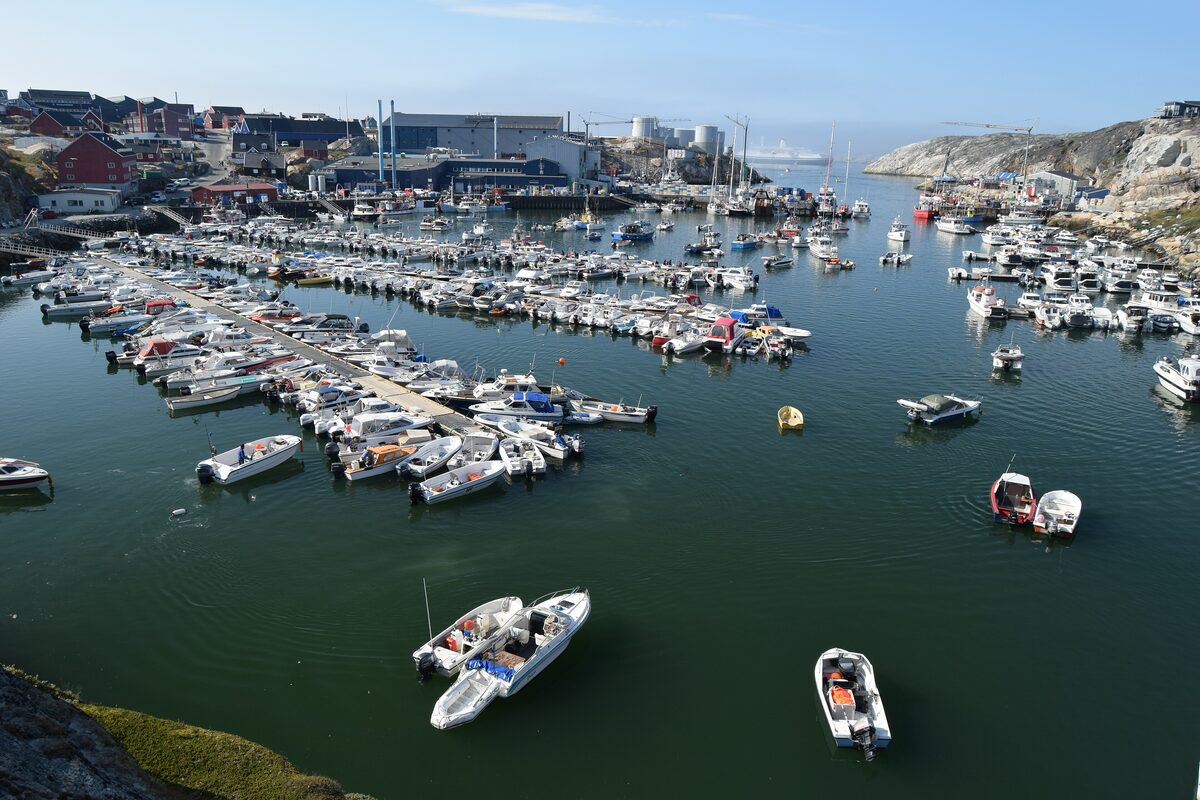 Small boats and fishing vessels moored in the Ilulissat harbor, with warehouses and storage tanks along the far shore