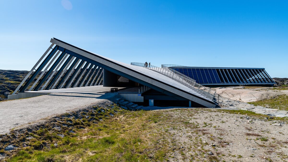 The Ilulissat Icefjord Centre, a low building with a long slanted roof of solar panels on the rock above the fjord